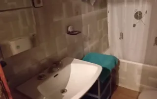 cuarto de baño con un lavabo de pedestal, un espejo, una bañera con una cortina estampada y un inodoro parcialmente visible