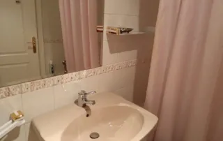 el interior de un baño, que incluye un lavabo, un espejo, una cortina de ducha y una puerta