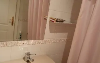 baño con un estilo que recuerda a las décadas de los 80 o principios de los 90, caracterizado por sus sanitarios de color rosa y azulejos blancos estándar.