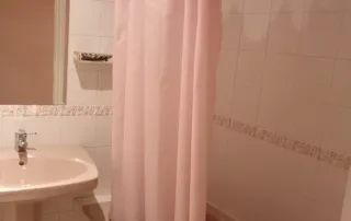 baño con un estilo que recuerda a las décadas de los 80 o principios de los 90, caracterizado por sus sanitarios de color rosa y azulejos blancos estándar.