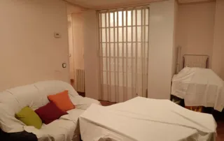 una sala de estar con un sofá y una mesa cubiertos con sábanas, lo que sugiere que la habitación está en proceso de mudanza, almacenamiento o limpieza.