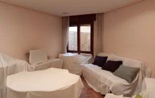 sala de estar con los muebles cubiertos por sábanas blancas. Este tipo de acción se realiza comúnmente para proteger los muebles del polvo y la suciedad durante un período de inactividad, una mudanza o una renovación.