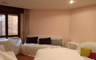 na sala de estar con varios muebles cubiertos con sábanas o protectores blancos, lo que sugiere que la habitación está en proceso de mudanza, almacenamiento o preparación para una renovación