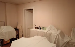 piso Las habitación con muebles cubiertos por sábanas o telas blancas, lo que sugiere que la habitación está en proceso de limpieza, renovación o almacenamiento.